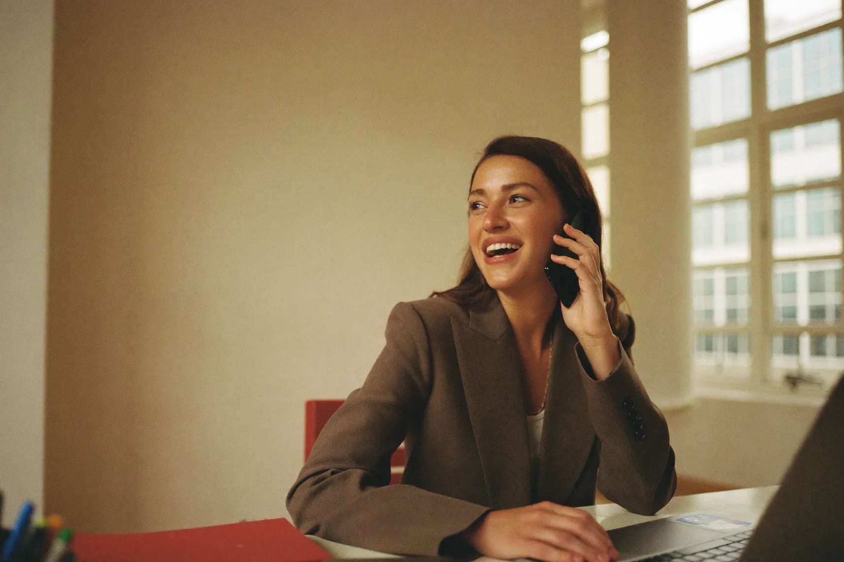 A professional in a tailored blazer smiling mid-call at her desk in a bright office