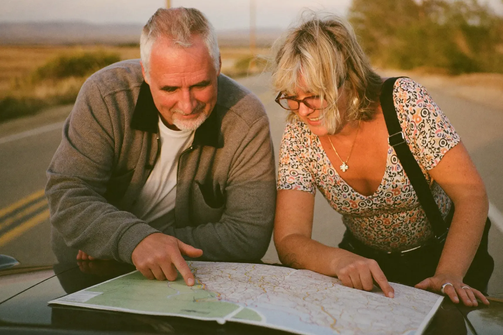 A couple studying a road map on the hood of their car at a scenic overlook